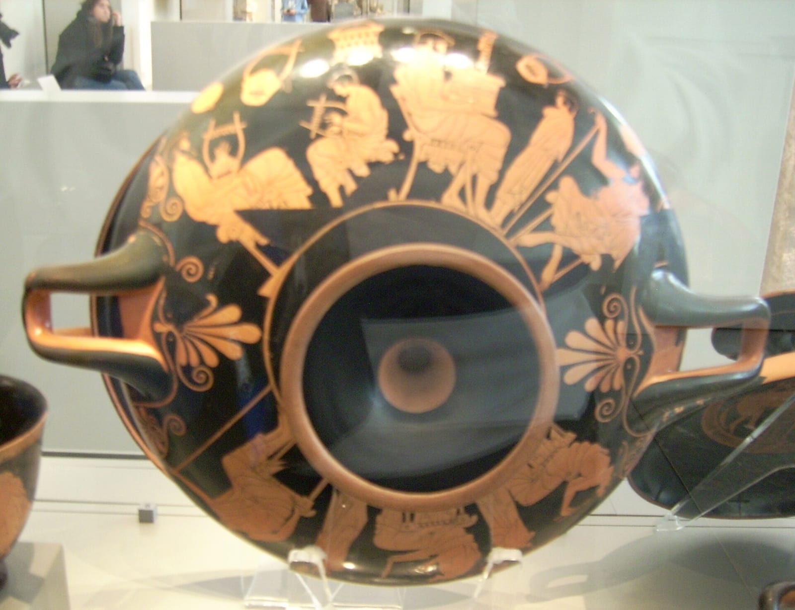 A shallow two-handled drinking cup seen from the side, painted in red-figure with seated teachers and standing pupils.