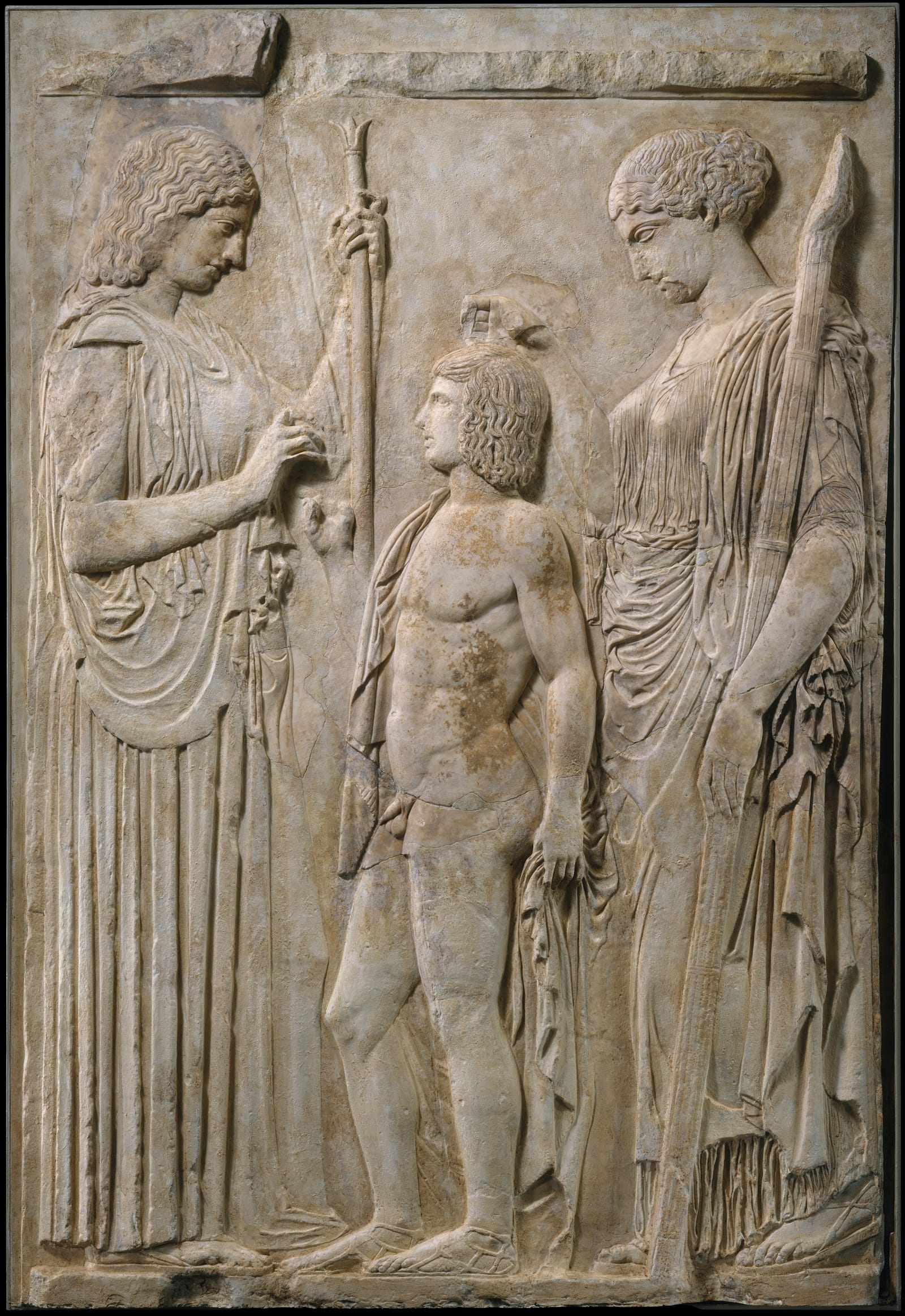 A marble relief: two tall women in long robes, Demeter and Persephone, stand on either side of a naked boy, Triptolemus.