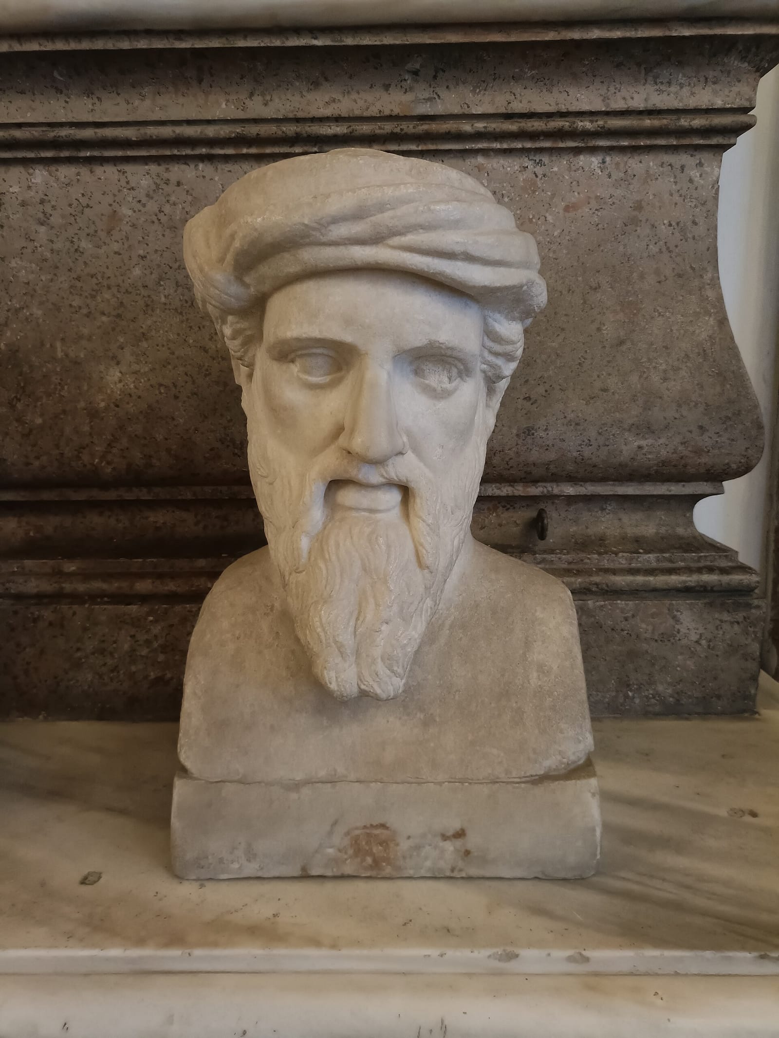 A marble bust of a bearded man wearing a soft cap or turban.
