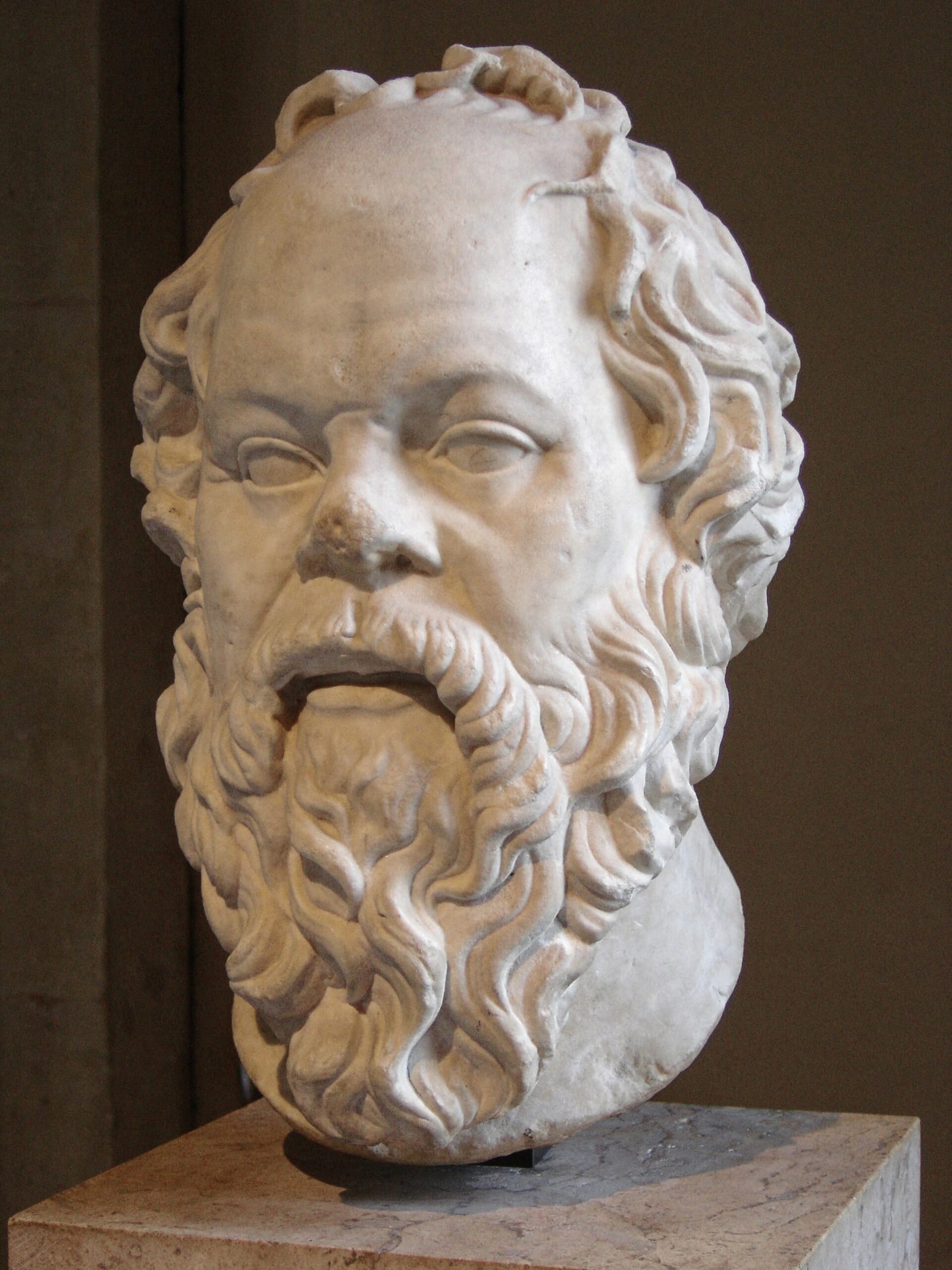A marble head of an old man with a broad flat nose, bulging eyes and a thick curly beard.